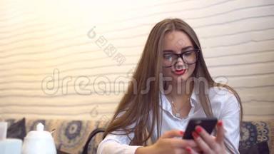 年轻的女商人戴着眼镜发短信，在智能手机上发短信，坐在咖啡馆里。 年轻漂亮的女商人